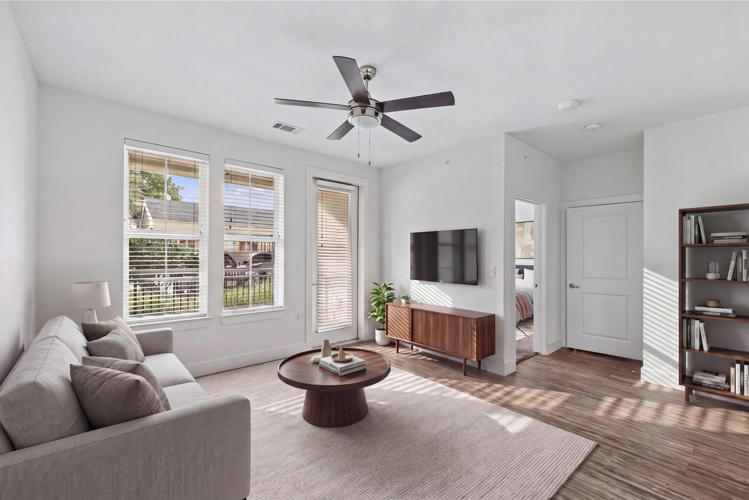 Sunlit living room at Embree Hill featuring wood-style flooring, large windows, and a private patio entrance.