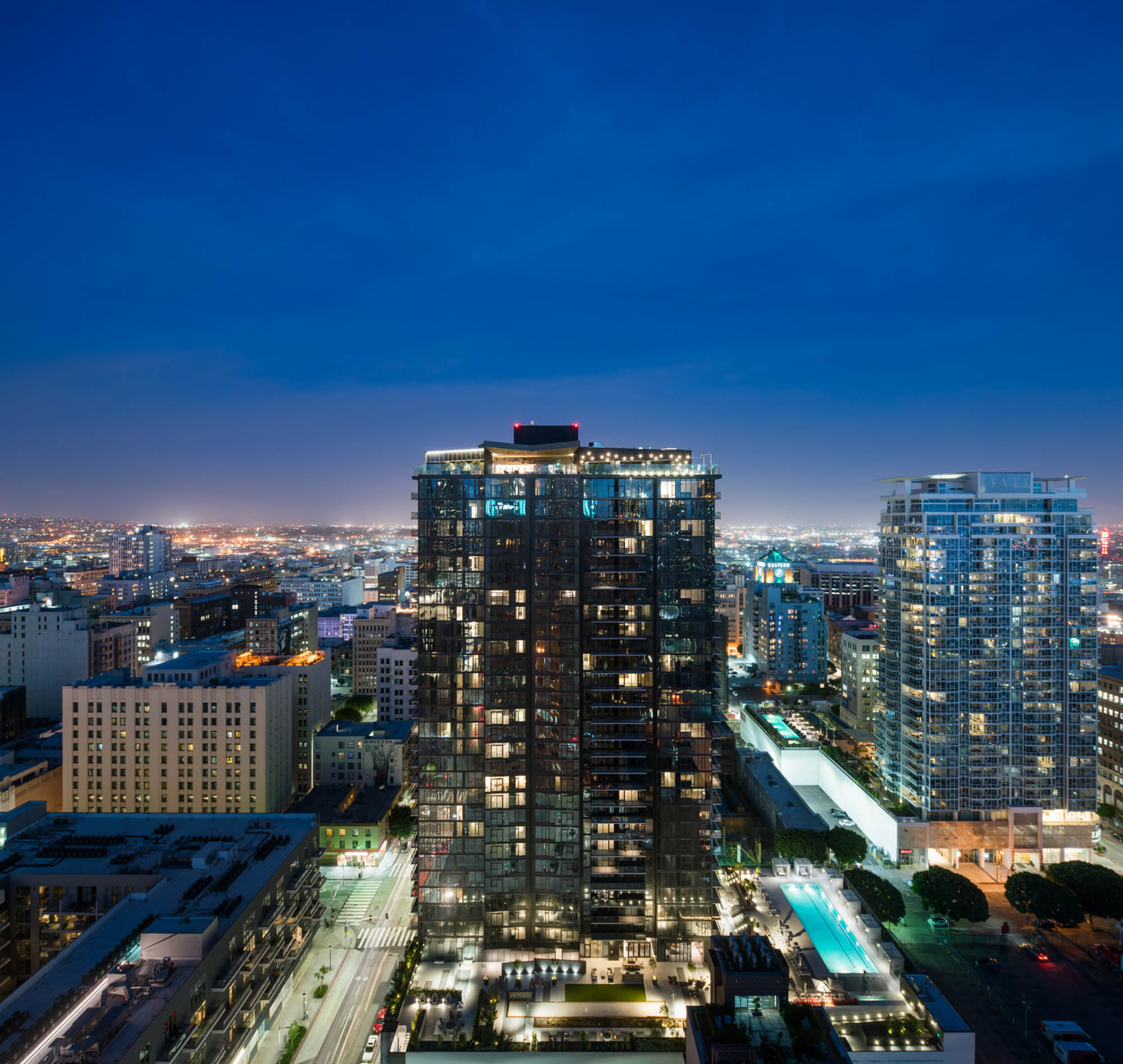 A rooftop level exterior image of the Atelier apartment building with vibrant buildings and the evening city skyline in downtown LA
