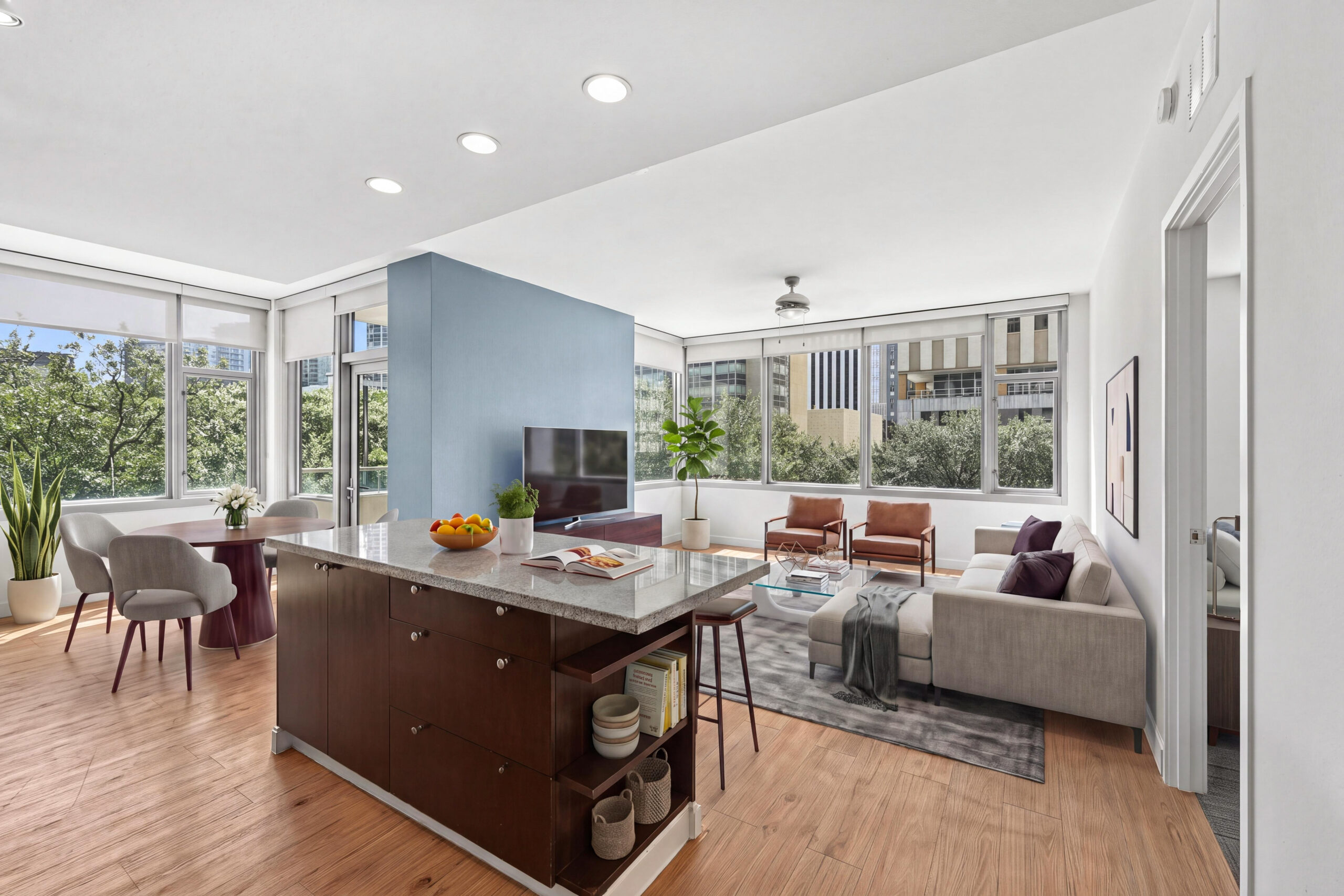 Open-concept apartment with a large kitchen island, dining area, modern living room and oversized windows overlooking downtown Dallas.