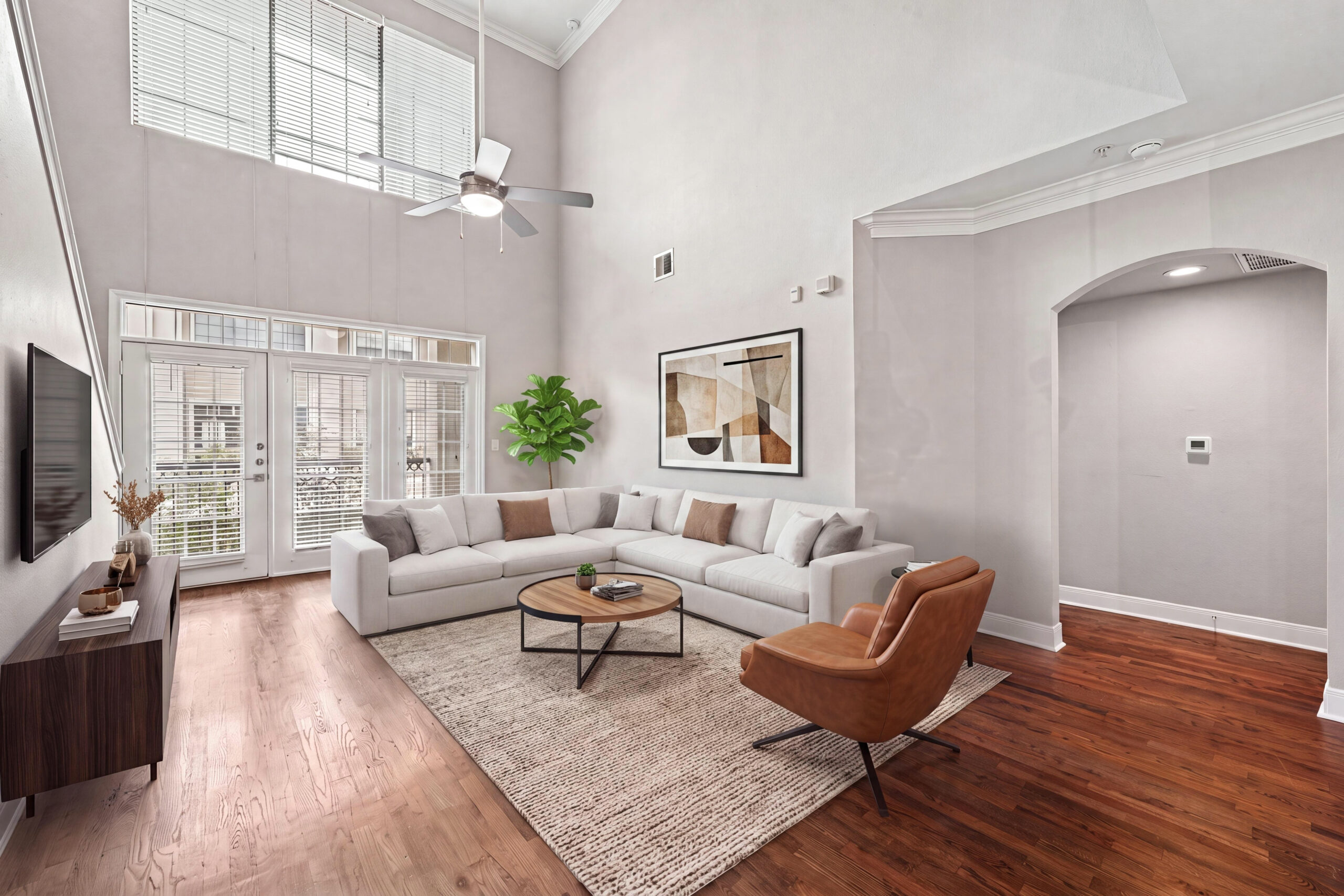 Open-concept living room at Village on Memorial featuring high ceilings, wood-style flooring, a ceiling fan, and a white kitchen with stainless steel appliances.
