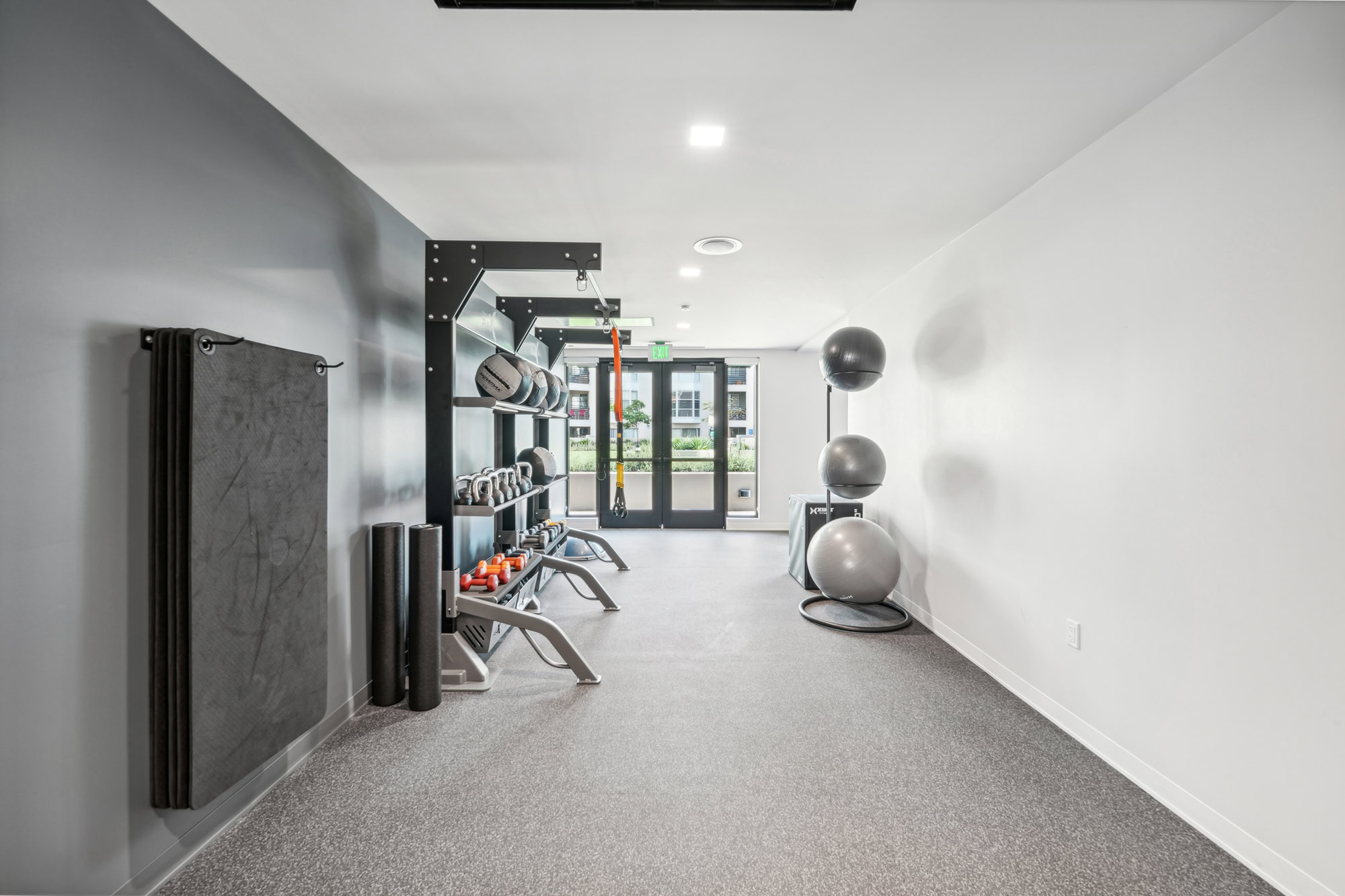 A monochrome fitness center with weights and medicine balls by an exit at Bayside Villages modern apartments in downtown San Francisco