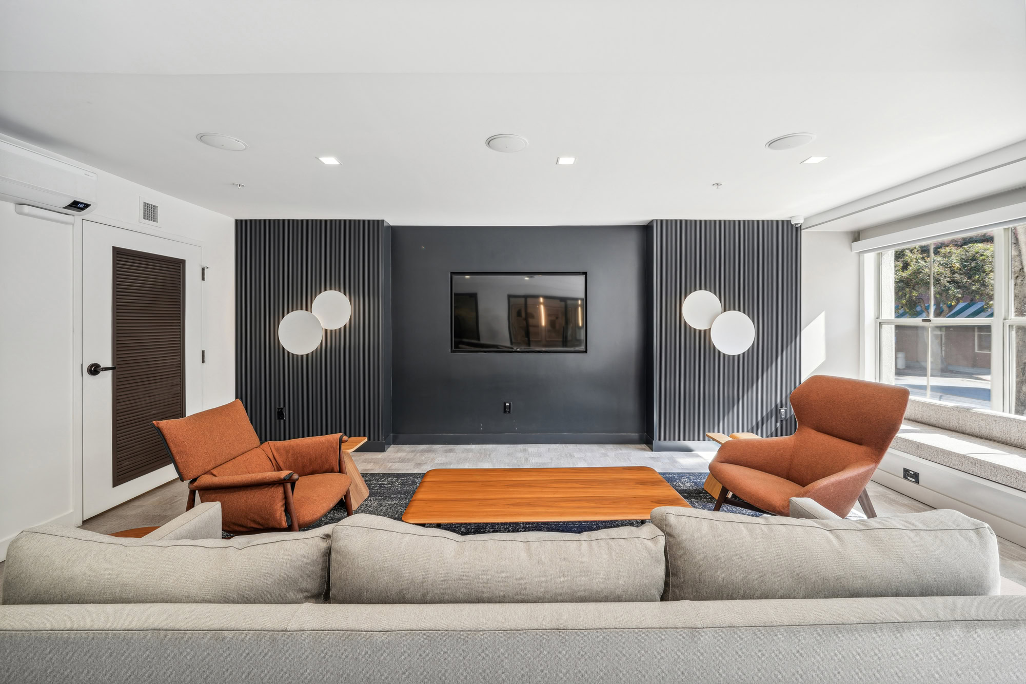 A modern lounge with a couch, chairs and tv on a black accent wall at Bayside Village apartments in downtown San Francisco