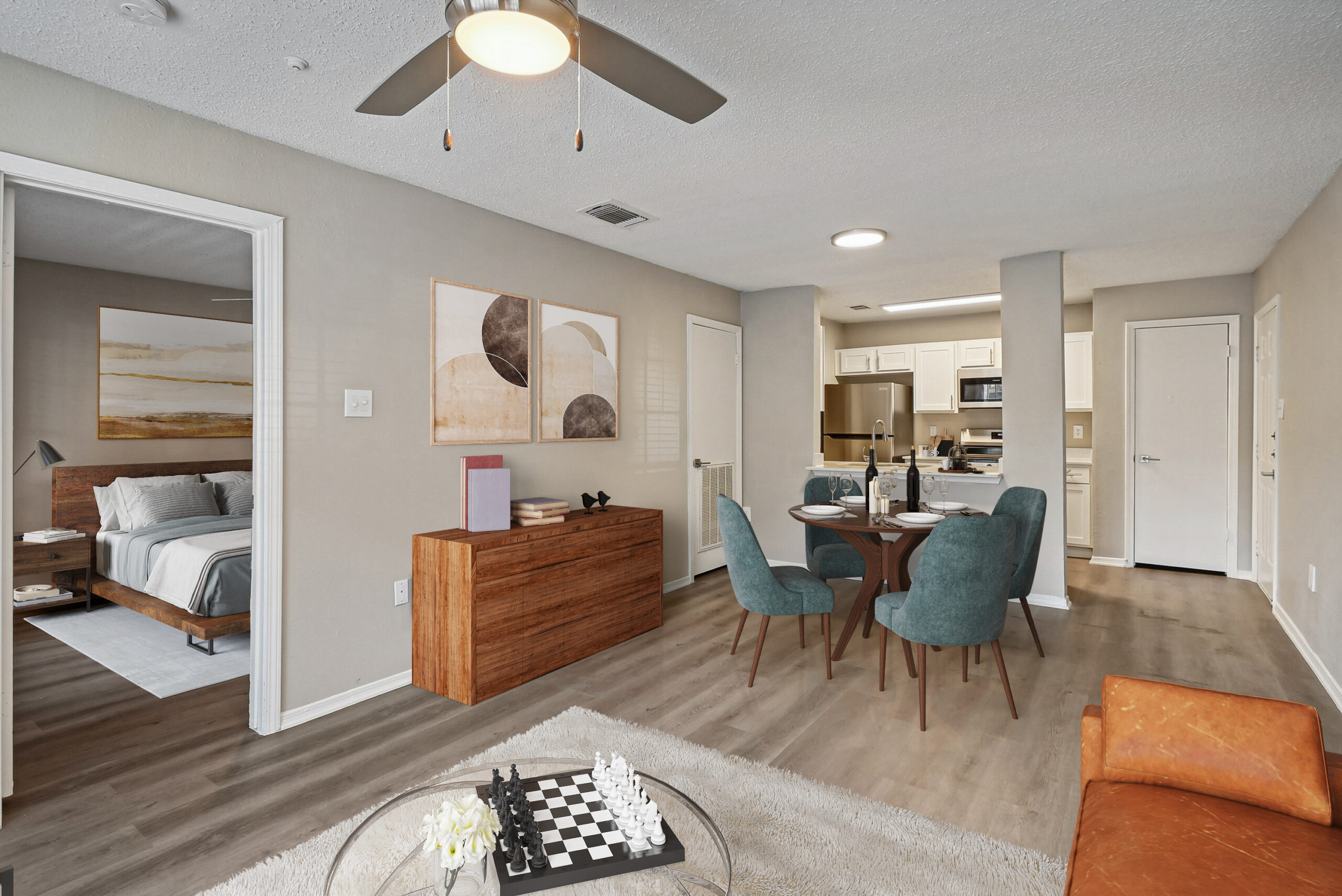 Modern open-concept living space with beige walls, featuring a kitchen and dining area with teal chairs, a cozy bedroom, and a chess set on the coffee table.