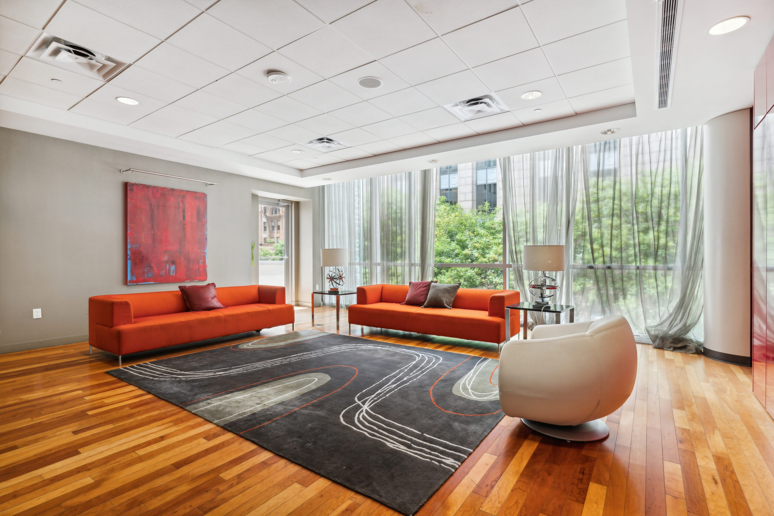 Modern lounge with bright orange couches, a window wall, wood flooring and a large carpet at The Wilson apartments in Dallas, Texas