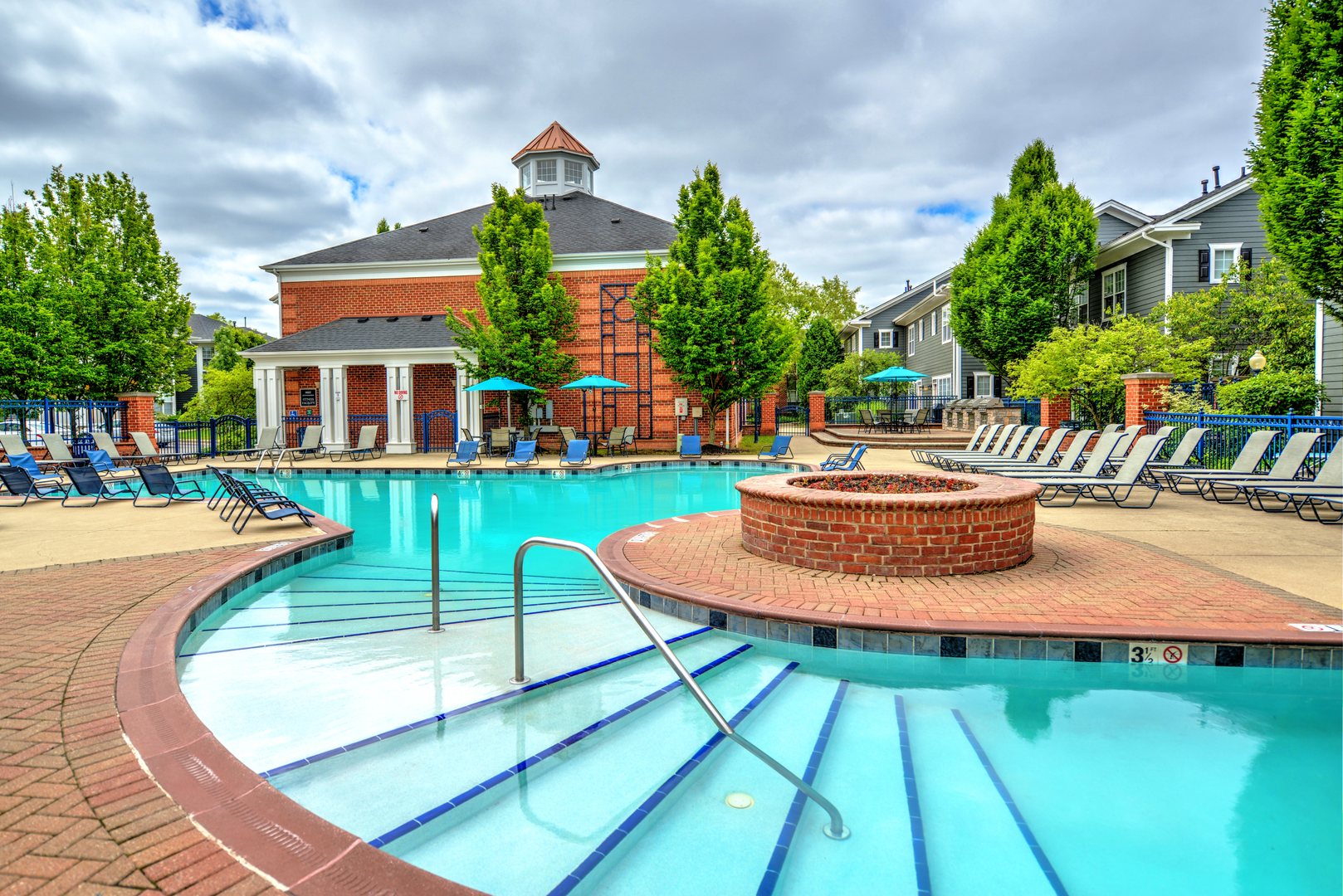 Outdoor swimming pool at LyvWell Apartments with lounge chairs, hot tub, and surrounding greenery in Columbus.