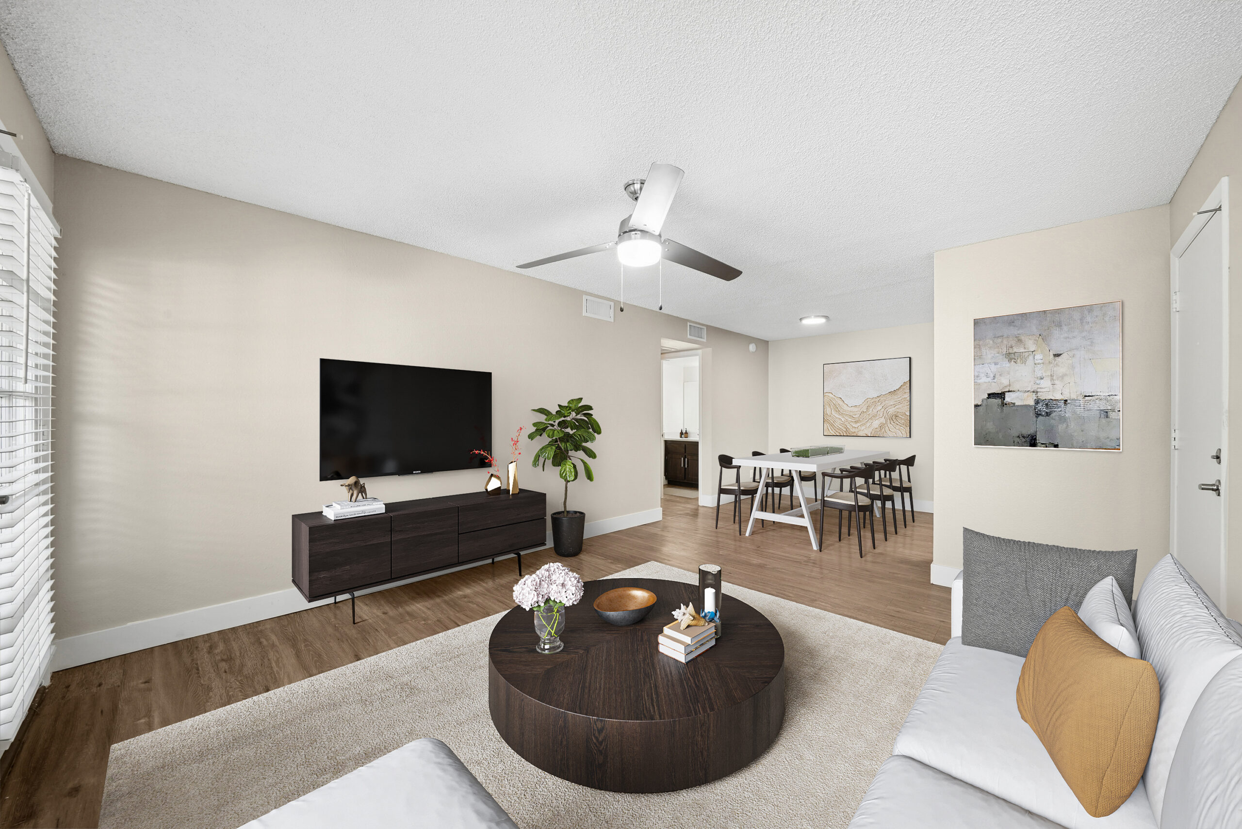 Contemporary living room at Arches at Hidden Creek with oak-style flooring, a ceiling fan and an adjoining dining area.