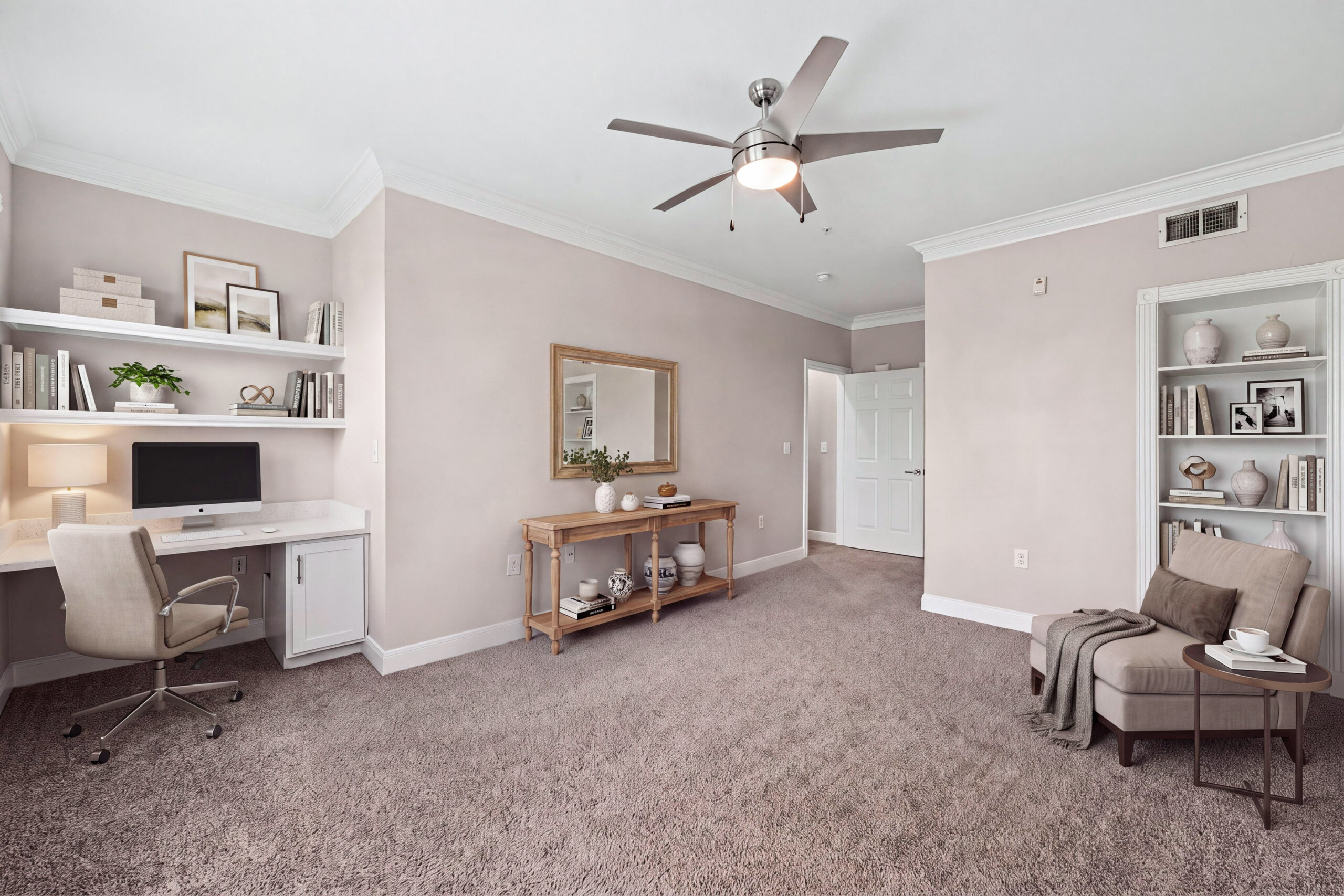 Flexible home office at Village on Memorial featuring a built-in desk, shelving, ceiling fan and a comfortable reading area.