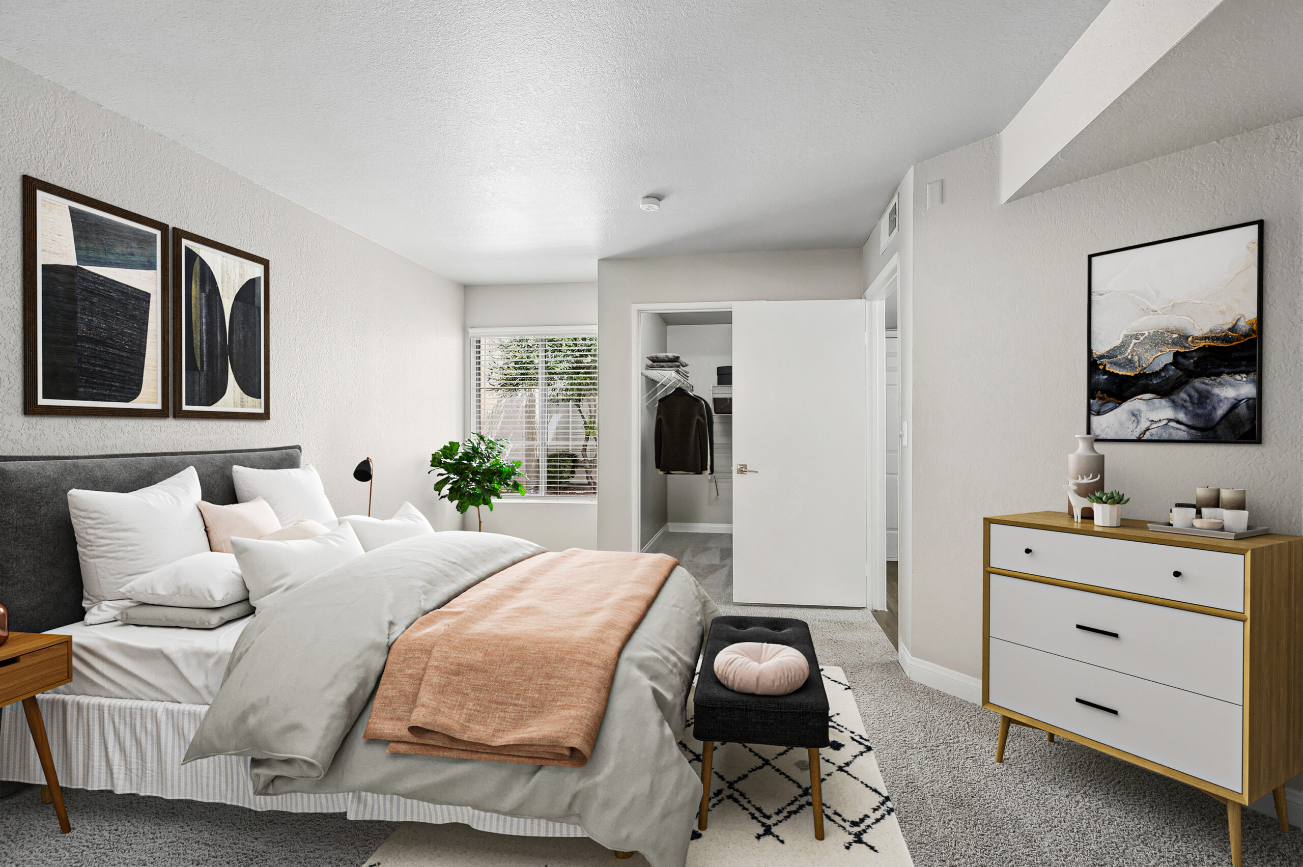 Carpeted apartment bedroom with a large window, upholstered bed, dresser, and walk-in closet.